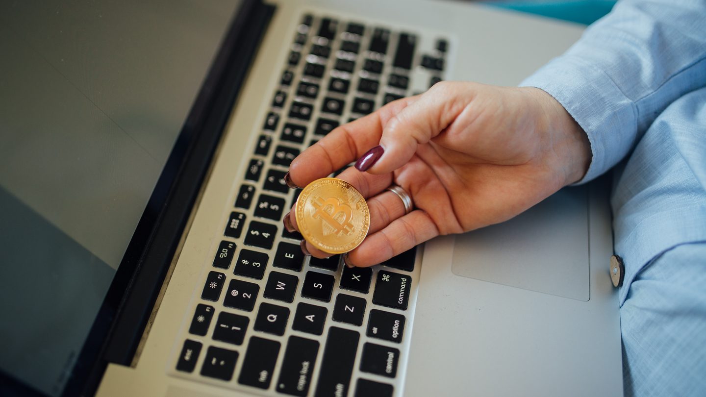A person holding a gold-coloured physical bitcoin token above a laptop