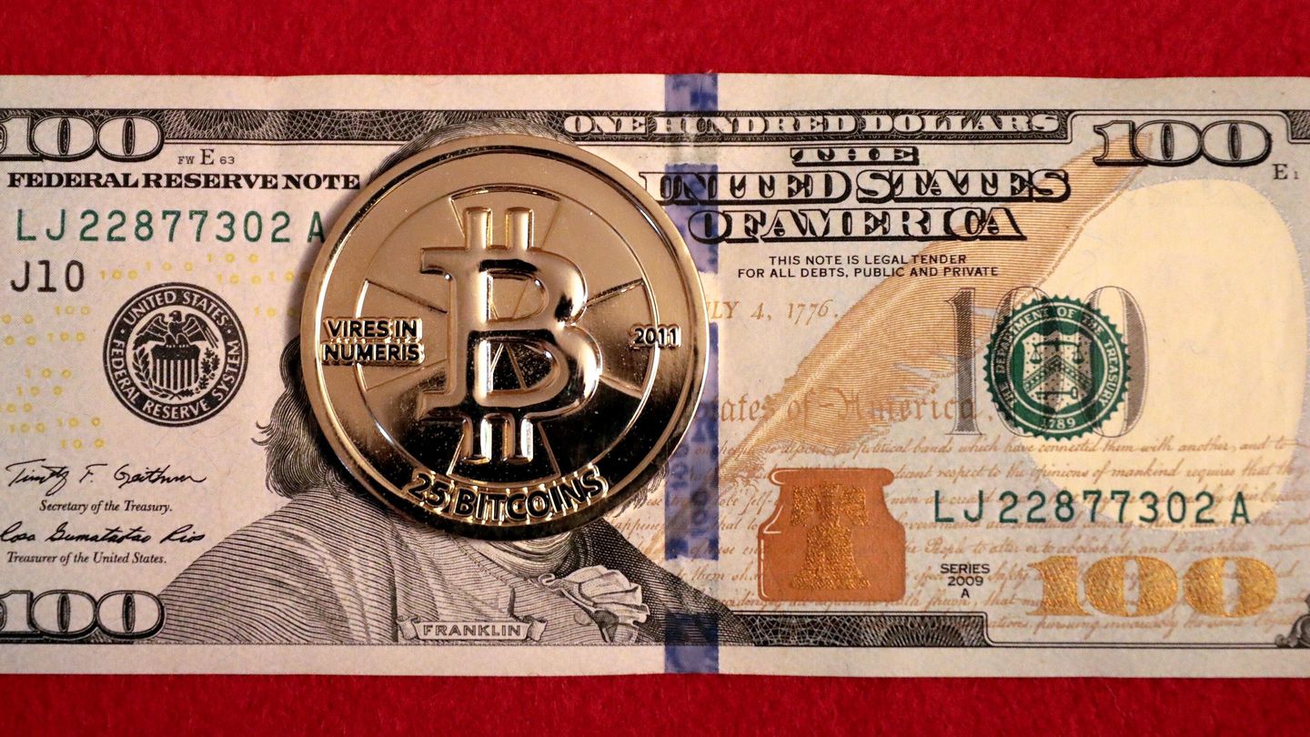 A gold-coloured physical bitcoin coin resting on a US $100 bill