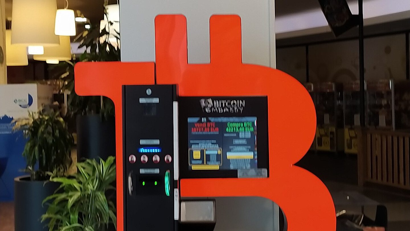 A bitcoin cash machine in front of a large orange bitcoin symbol inside a shopping centre
