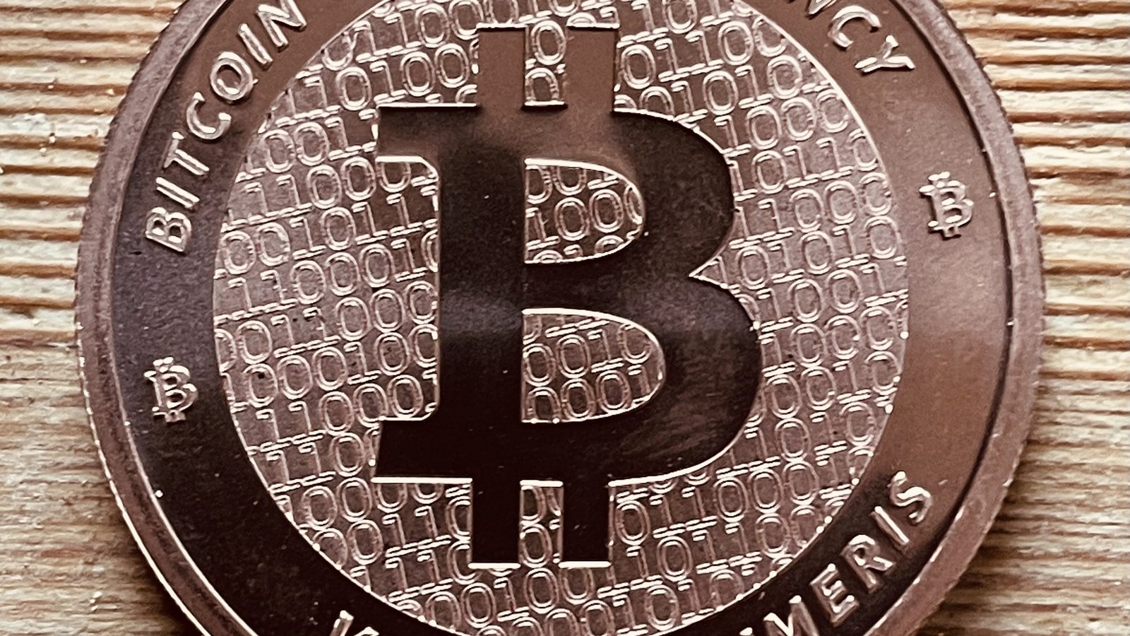Close-up of a copper-coloured bitcoin coin with a large B symbol on a wooden surface