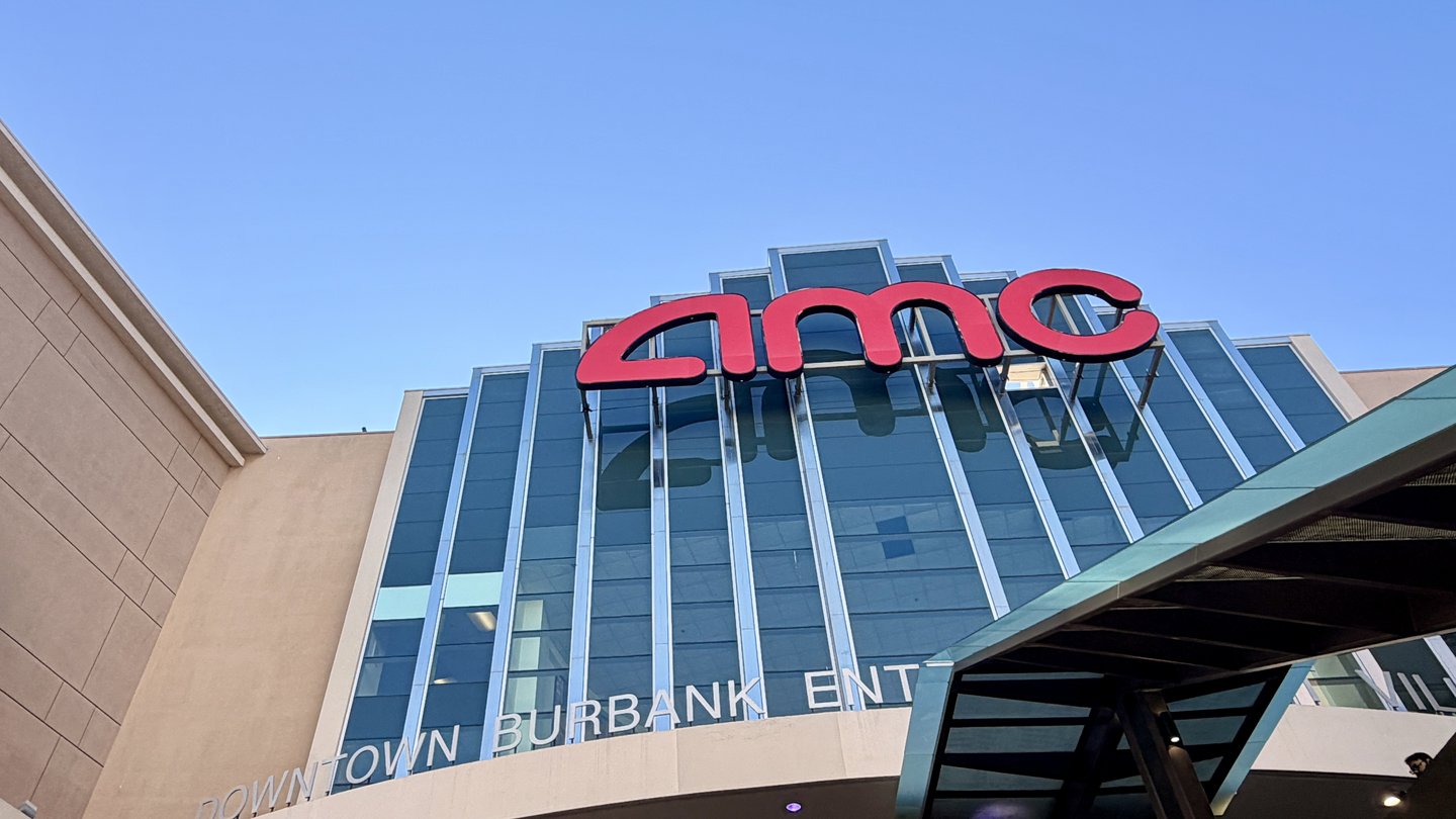 The red AMC sign on the glass front of the AMC Burbank 16 cinema in Burbank, California, under a blue sky