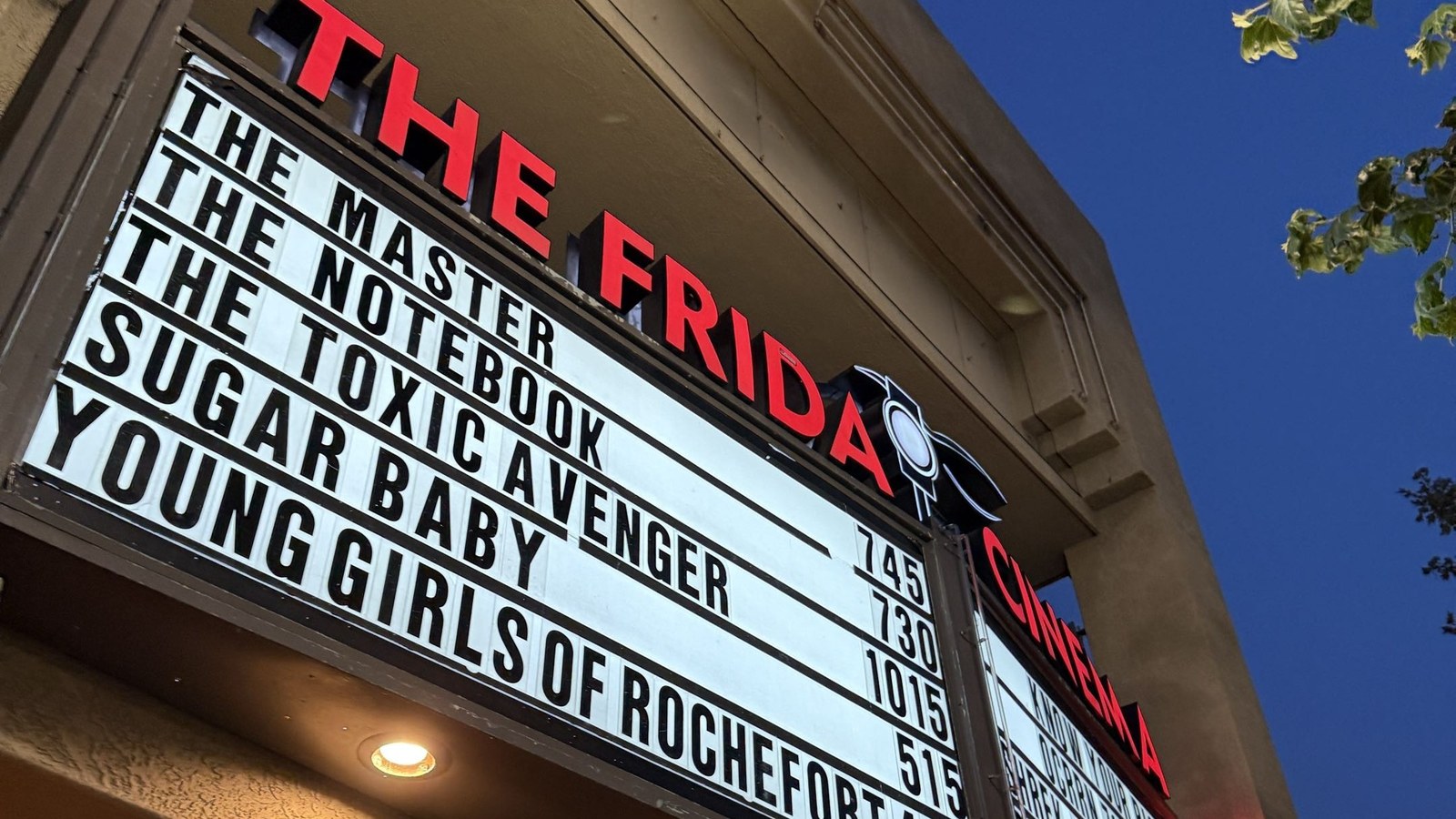 Illuminated marquee of The Frida Cinema with red lettering and film titles at dusk