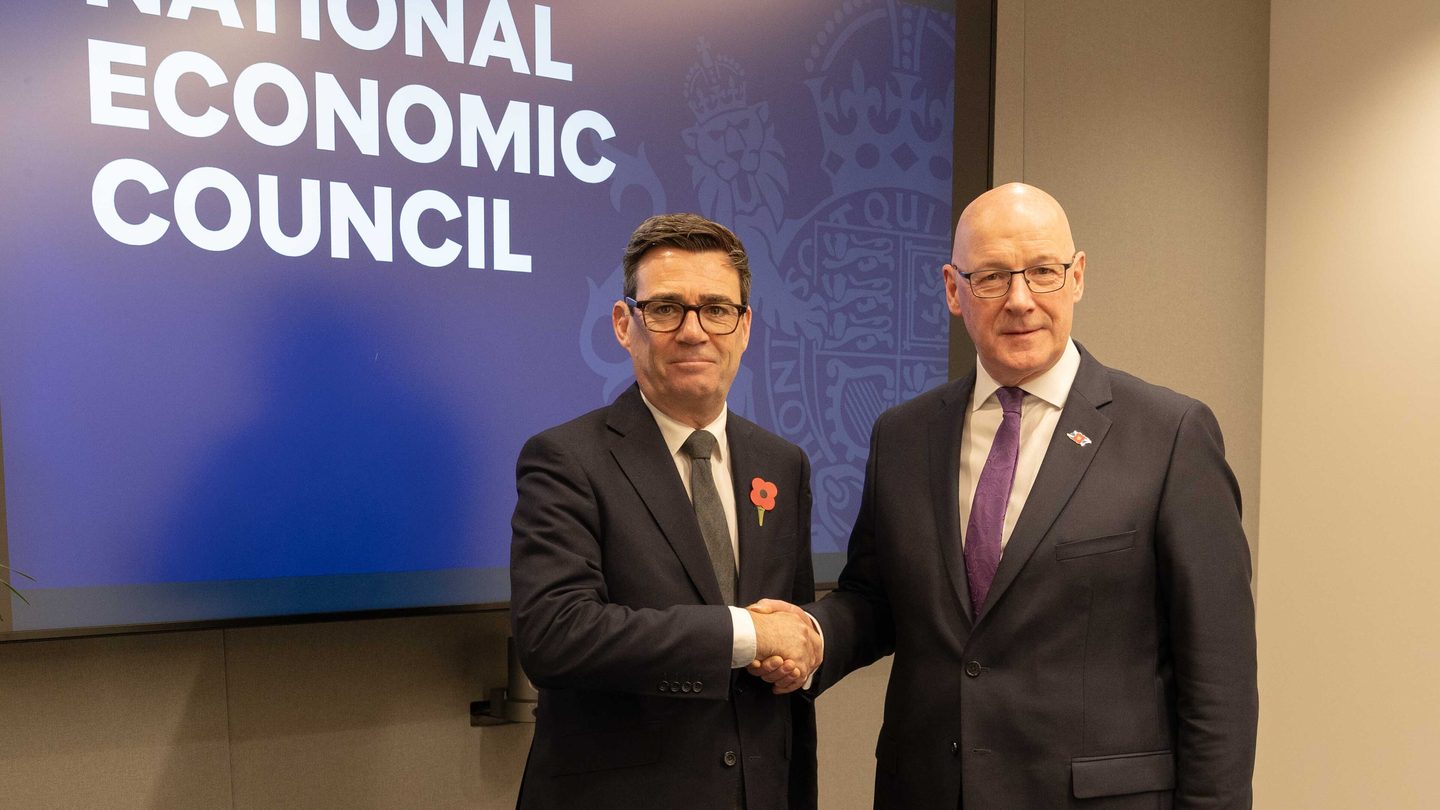 UK Prime Minister Andy Burnham shakes hands with Scotland's First Minister John Swinney in front of a National Economic Council screen