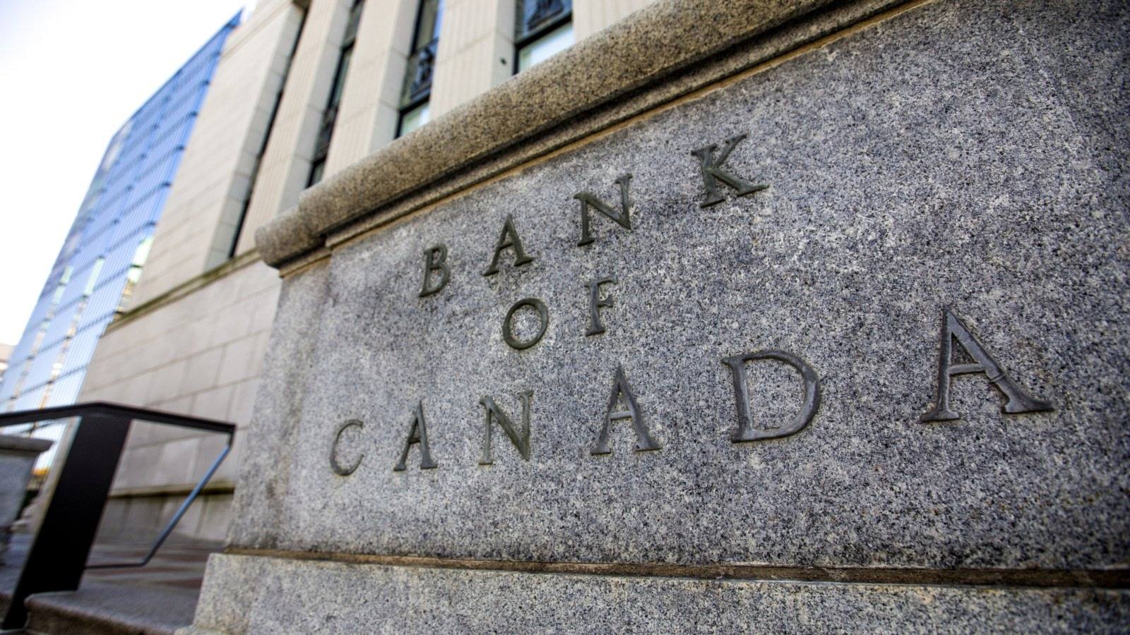 The words Bank of Canada carved into the stone corner of the bank's head office building in Ottawa, with a glass tower behind