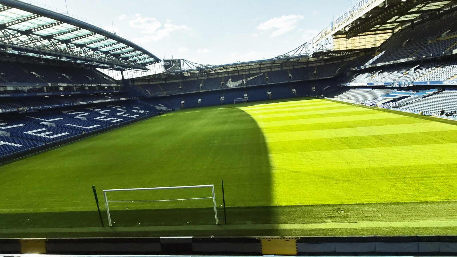 Pitch-level view of Stamford Bridge in London, with the goal in front of empty blue seats on a sunny day