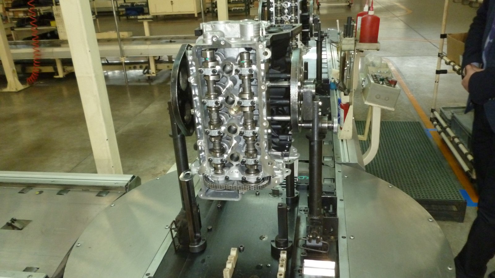 A car engine block on a turntable on a factory production line, with machinery and a red fire extinguisher in the background
