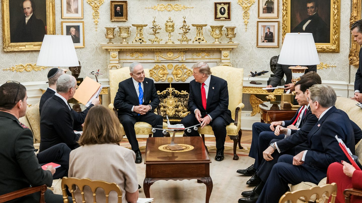 Israeli Prime Minister Benjamin Netanyahu and US President Donald Trump seated side by side in the Oval Office, surrounded by officials on sofas and chairs
