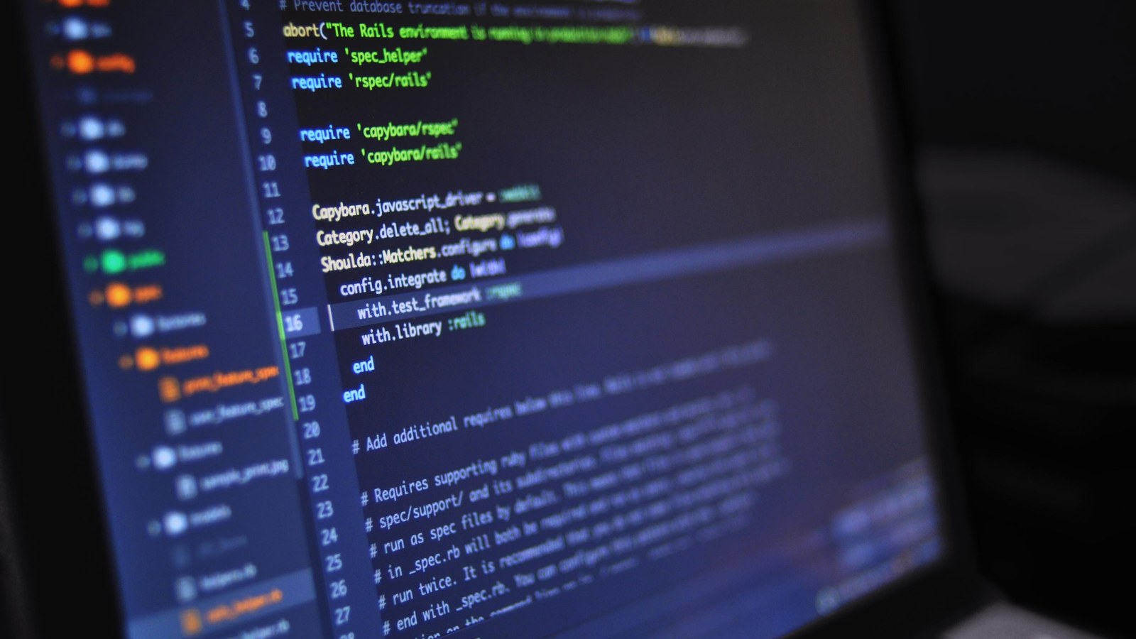 Lines of colour-highlighted source code on a laptop screen in a dark room