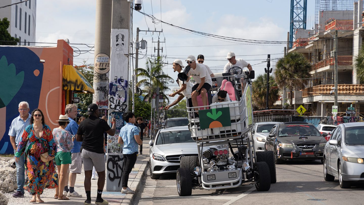 An Instacart-branded vehicle shaped like a giant shopping cart, with people riding on it, on a street in Miami
