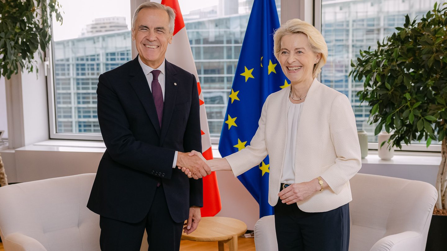 Canadian Prime Minister Mark Carney and European Commission President Ursula von der Leyen shake hands in front of Canadian and EU flags