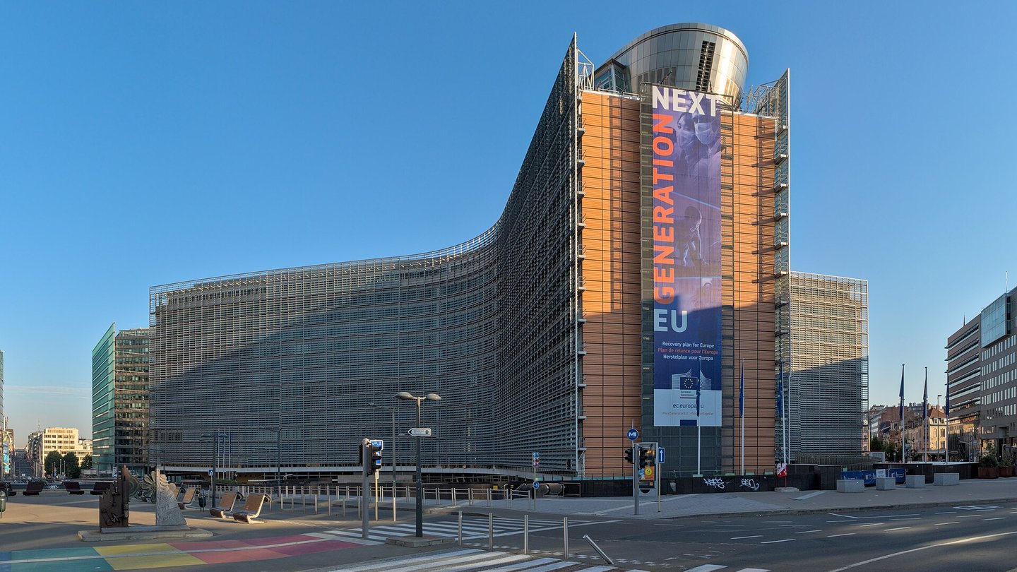 The curved glass facade of the Berlaymont building, headquarters of the European Commission, with a large banner, under a clear blue sky