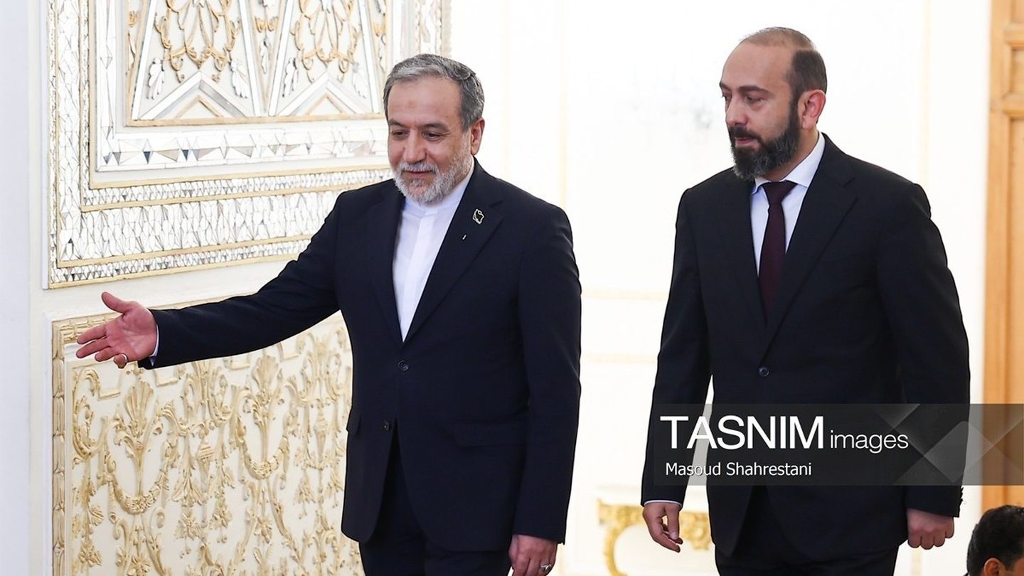 Iranian Foreign Minister Abbas Araghchi, in a dark suit, gestures with his right hand as he walks beside Armenian Foreign Minister Ararat Mirzoyan in an ornate white and gold hall in Tehran