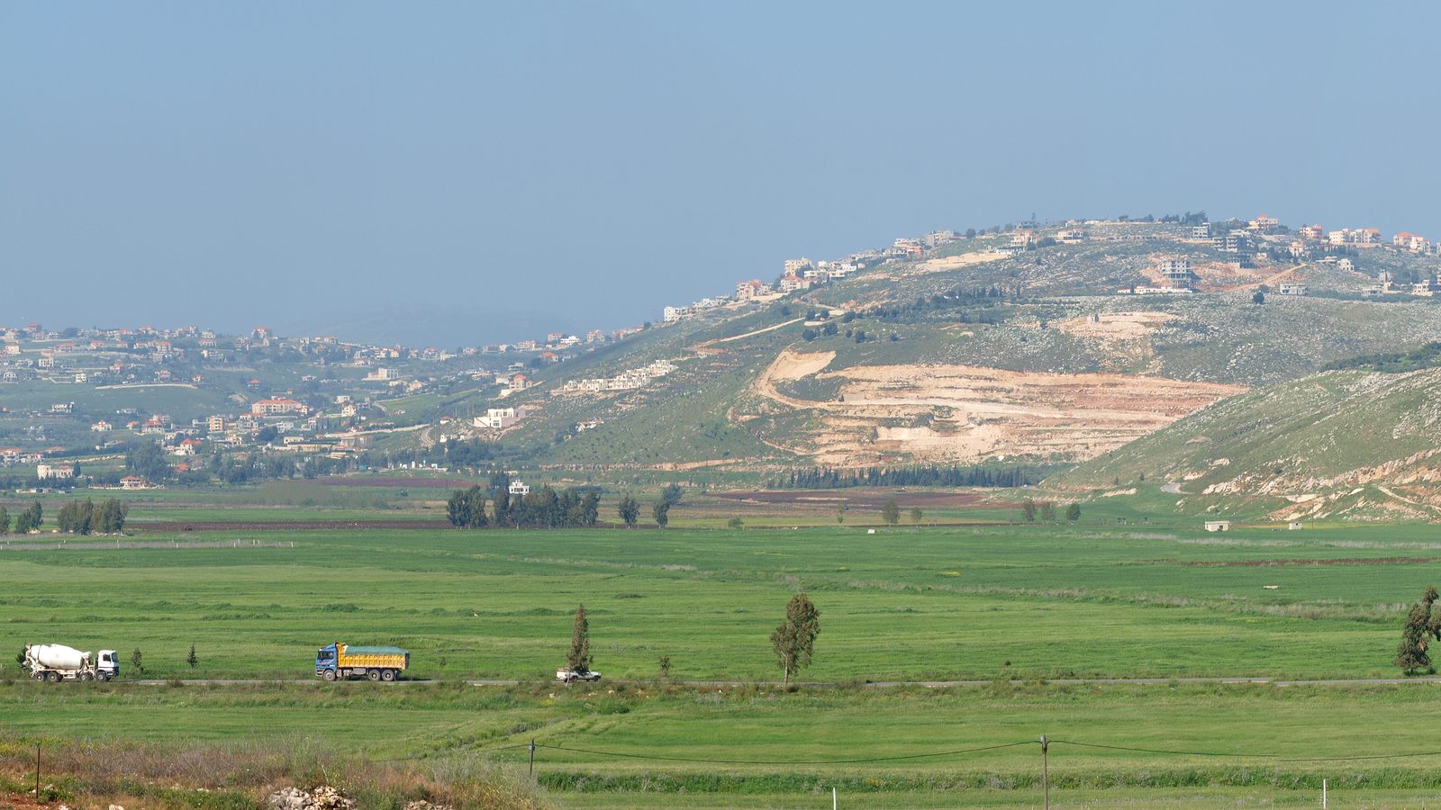 Green farmland in the foreground with the hilltop town of Khiam in southern Lebanon behind it