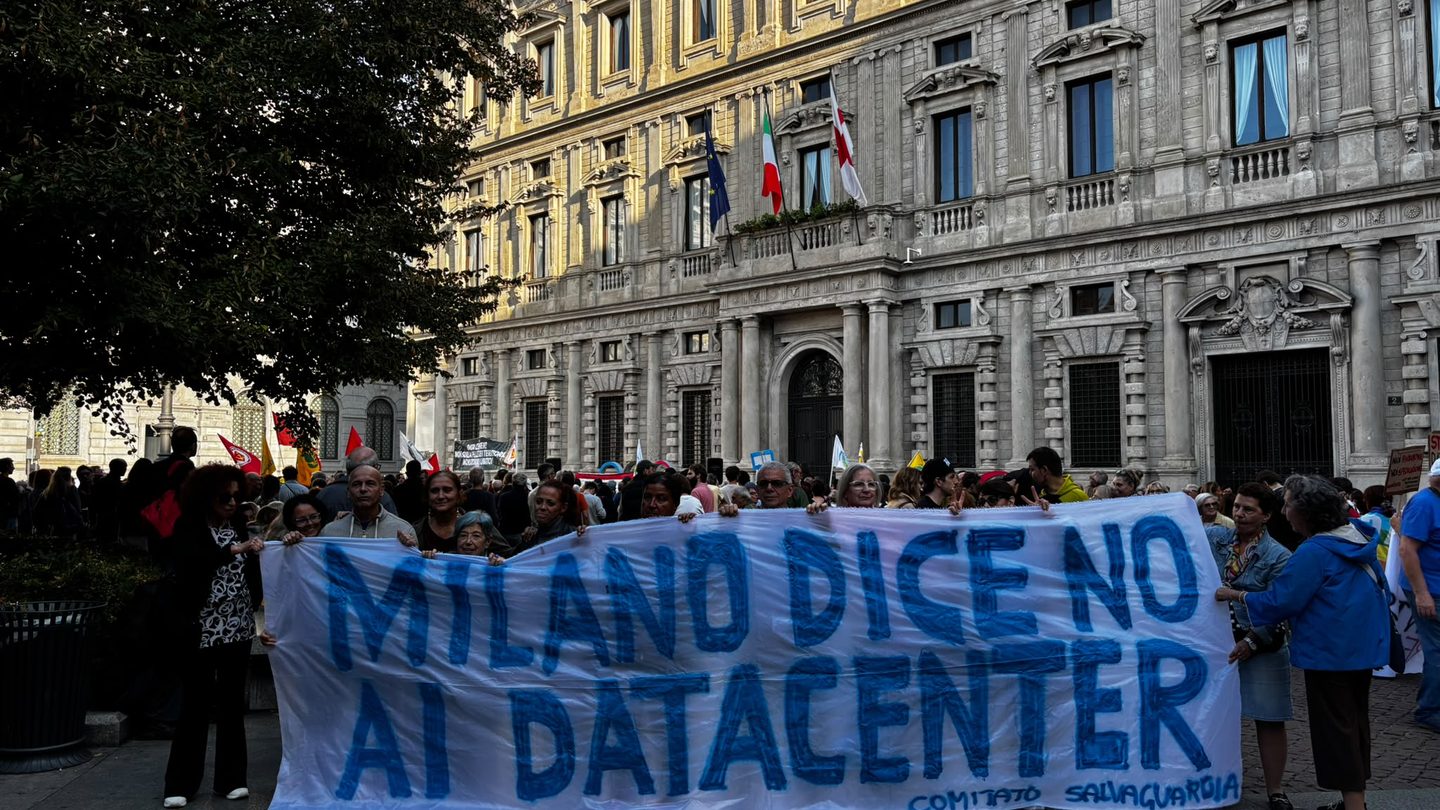 Protesters hold a large blue banner reading 'Milano dice no ai datacenter' in Piazza della Scala, Milan, in front of a historic palazzo