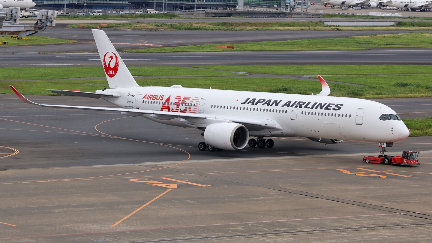 A white Japan Airlines Airbus A350 with a red crane logo on its tail being towed across the apron at Tokyo Haneda airport