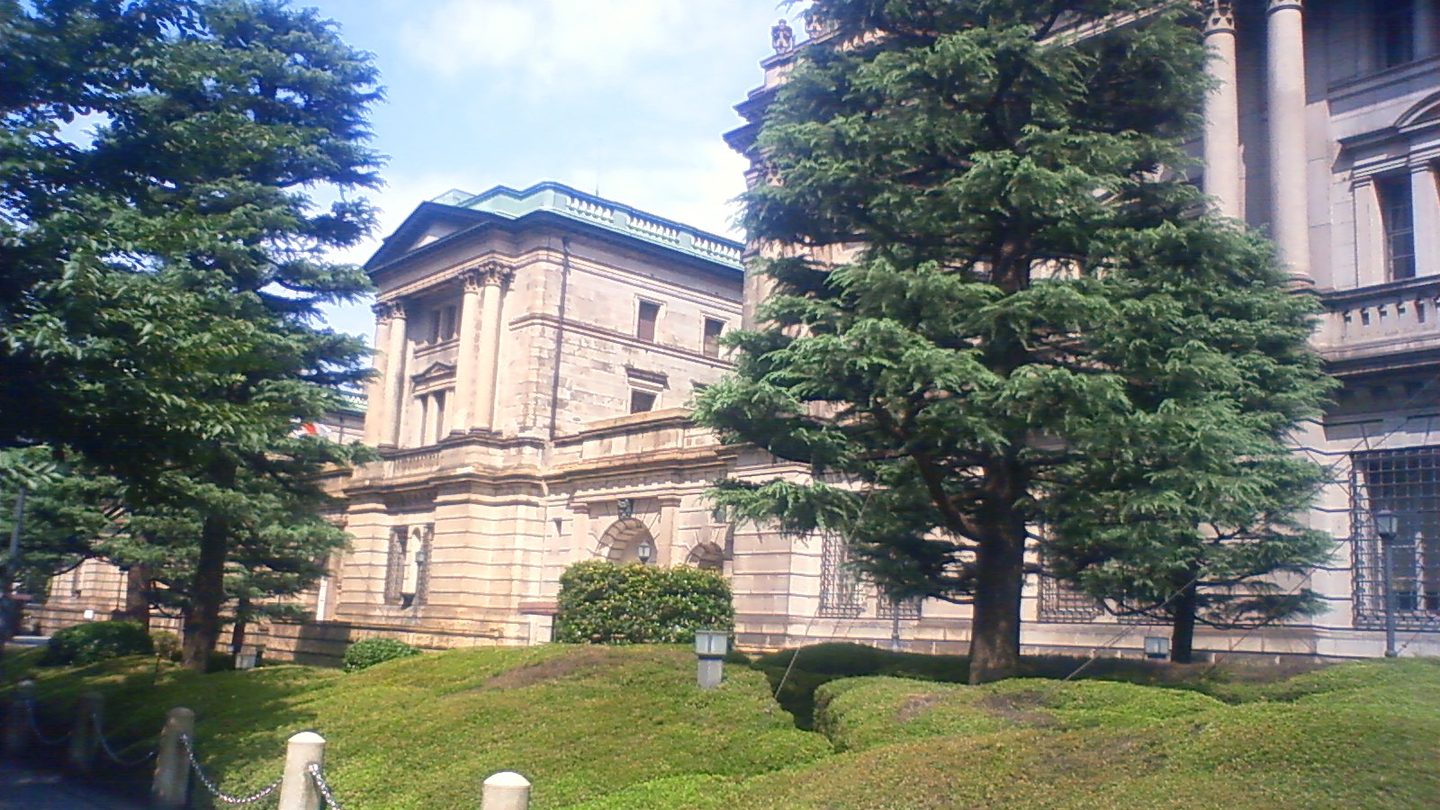 The stone main building of the Bank of Japan head office behind trees and a lawn