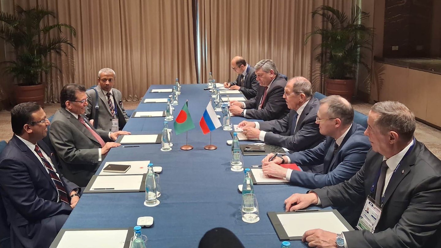 Russian Foreign Minister Sergei Lavrov, in glasses and a dark suit, sits with his delegation at a long blue-covered table with Russian and Bangladeshi flags during talks