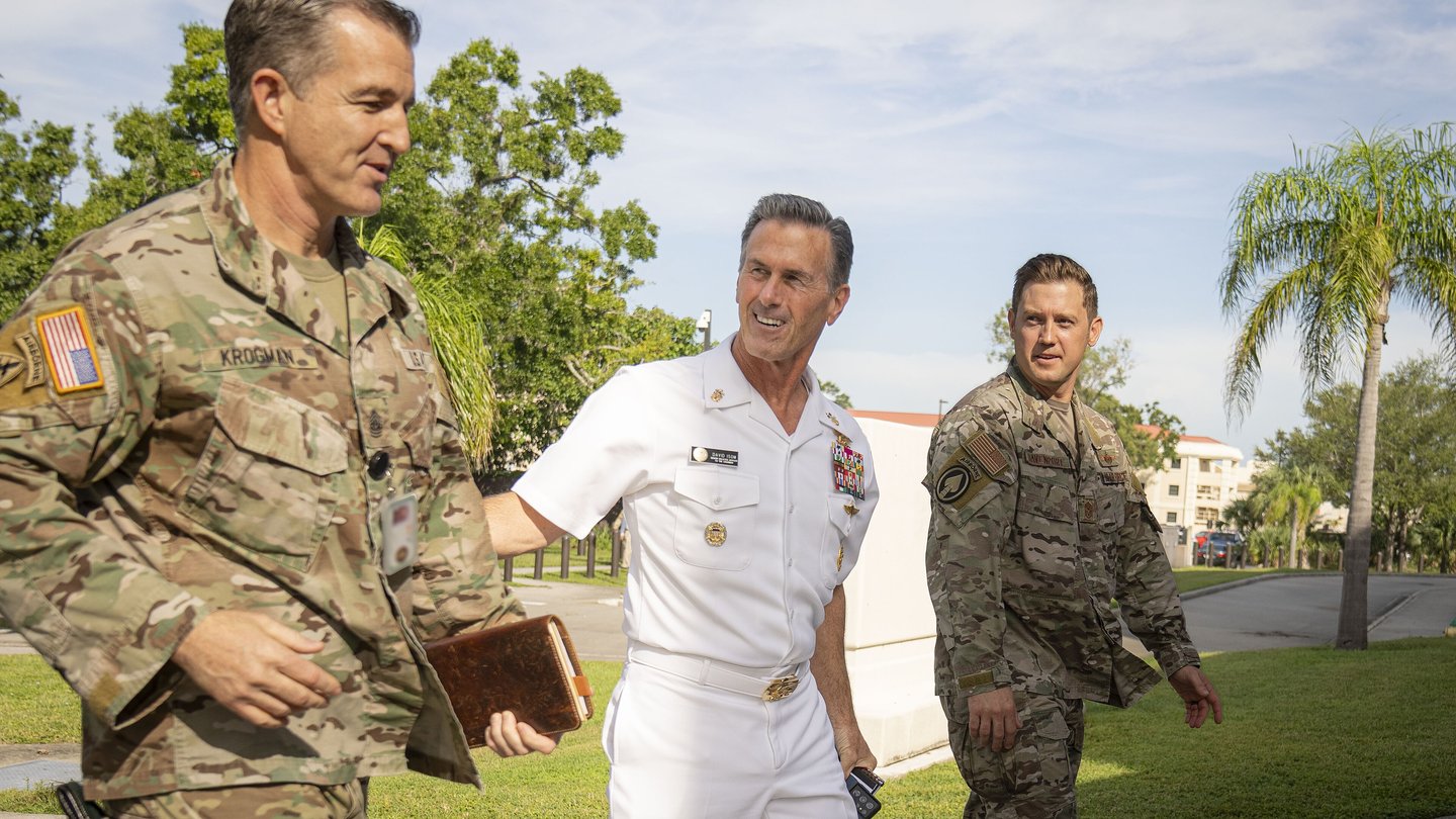 US Navy Admiral Brad Cooper in white uniform walks with two officers in camouflage uniforms outside US Central Command headquarters in Tampa