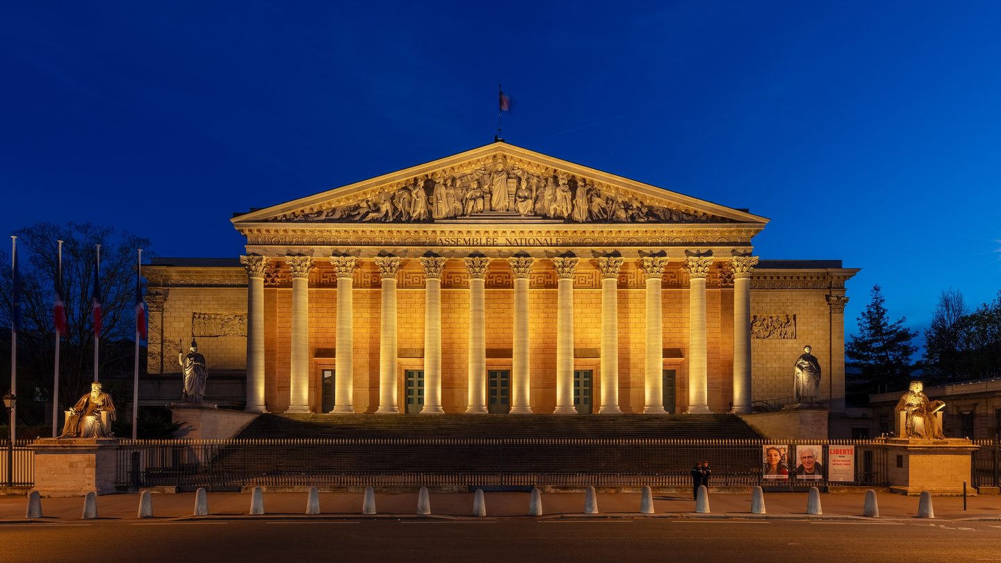 The Palais Bourbon, home of the French National Assembly, lit up at dusk on the banks of the Seine in Paris