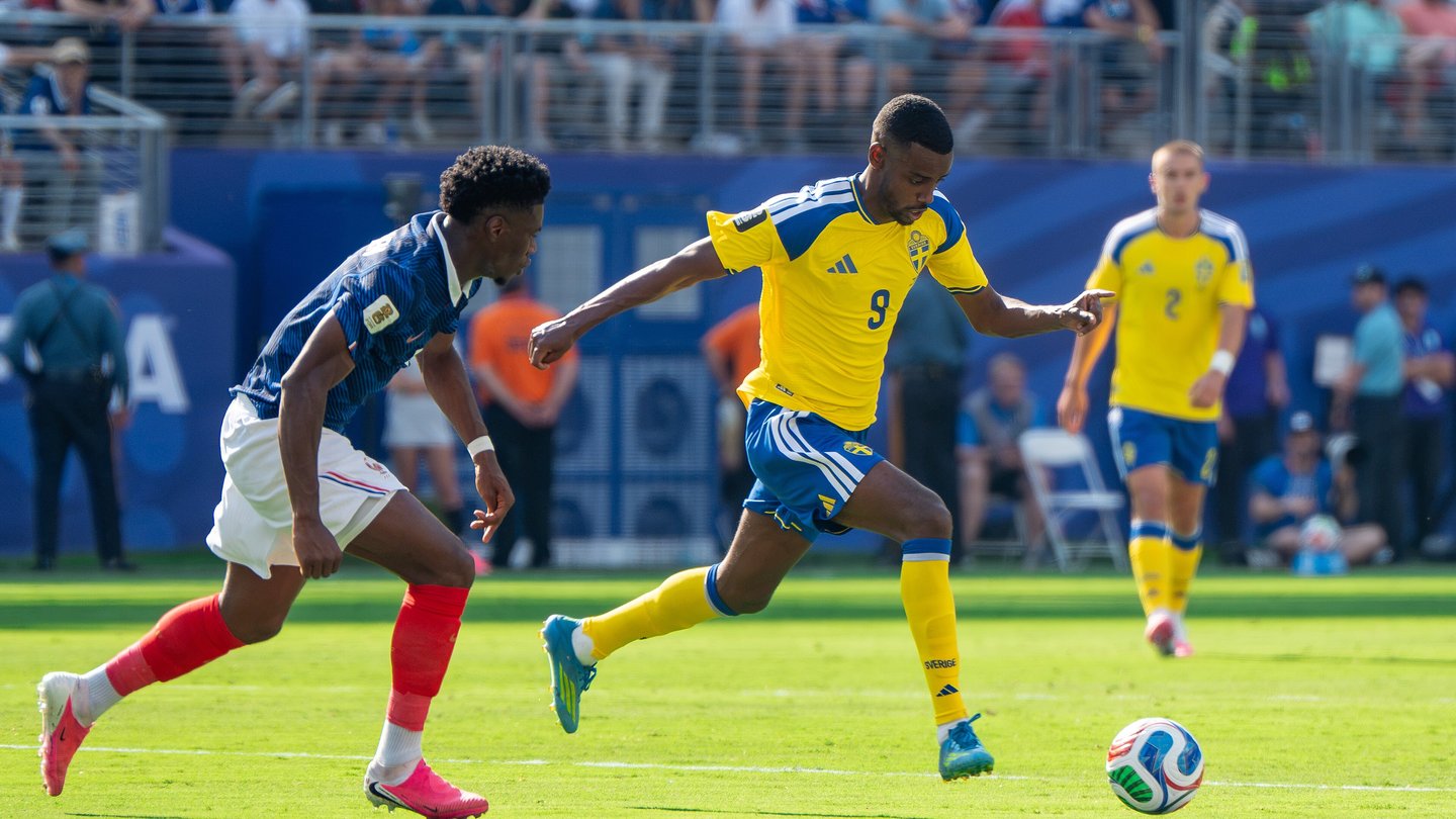 Alexander Isak in a yellow Sweden shirt running with the ball as a France player in a dark blue kit chases him