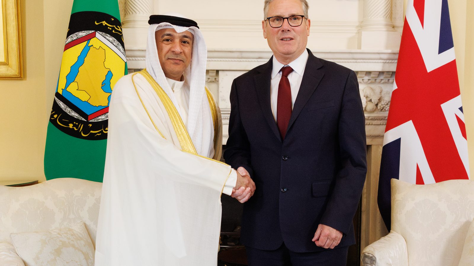 GCC Secretary General Jasem Mohamed Albudaiwi, in white Gulf dress, shakes hands with Keir Starmer, then UK Prime Minister, in front of GCC and UK flags