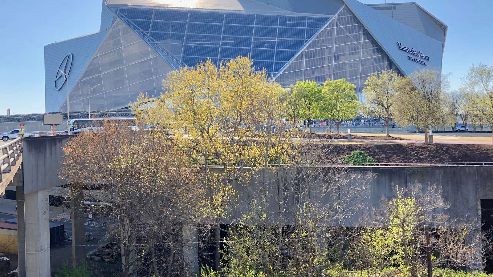 Exterior of the Mercedes-Benz Stadium in Atlanta with its angled glass facade, trees in the foreground