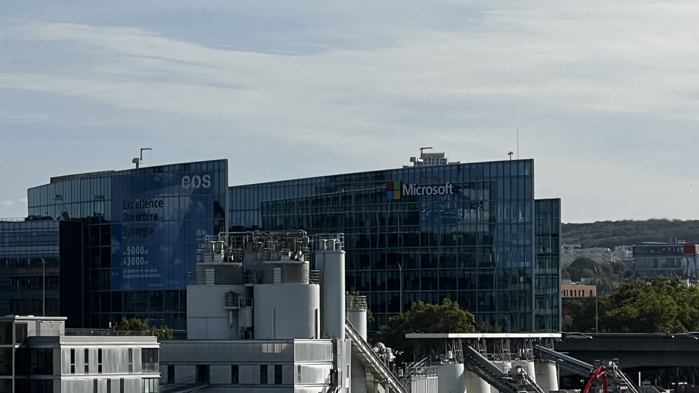 Glass office buildings with the Microsoft logo and name on the facade of the company's French headquarters in Issy-les-Moulineaux, near Paris, under a pale blue sky