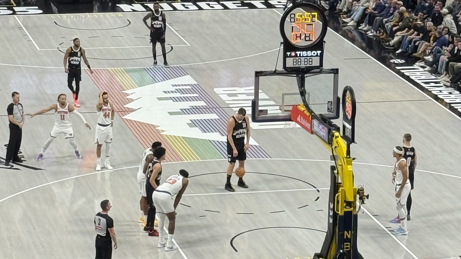 Nikola Jokic in a black Denver Nuggets jersey with the number 15 at the free-throw line at Ball Arena, with New York Knicks players lined up along the lane