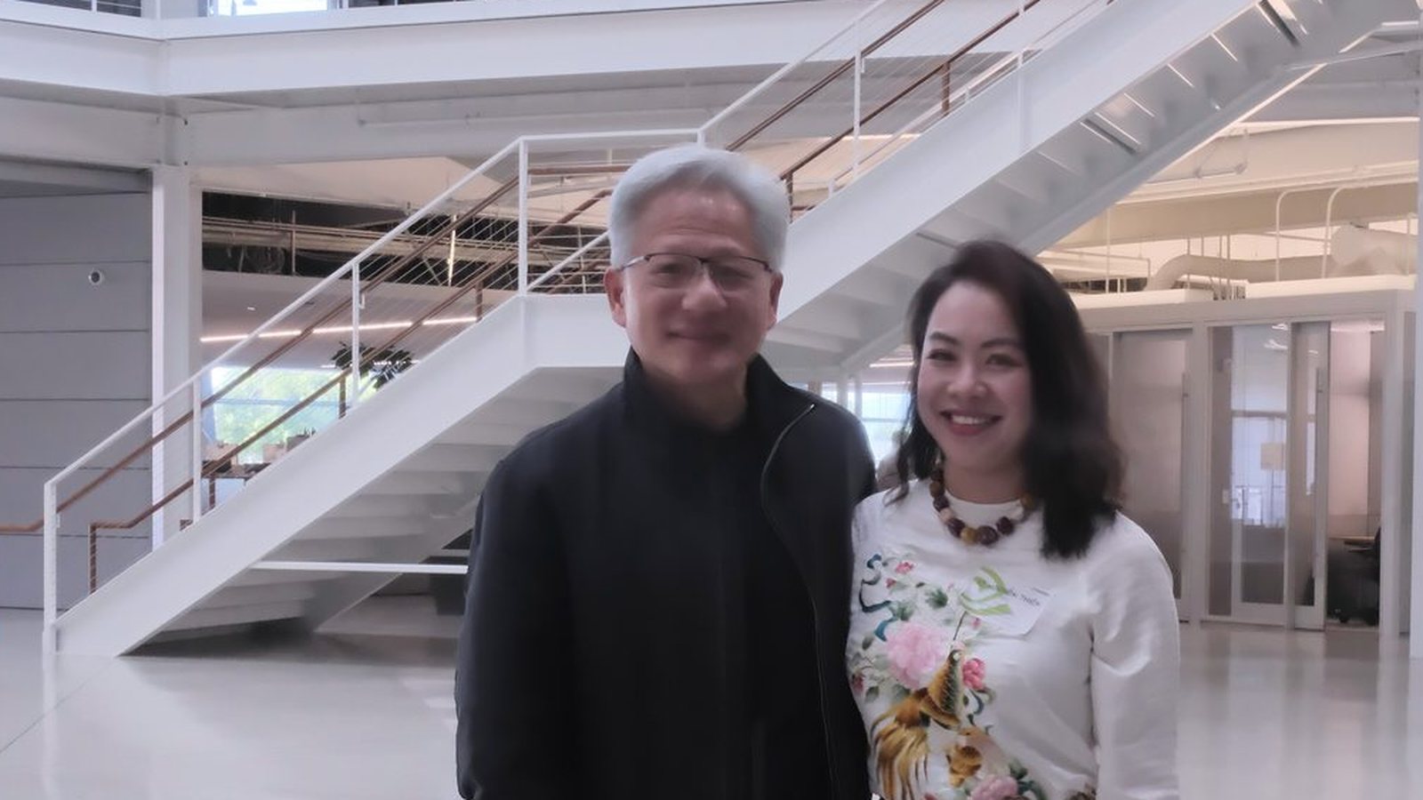 Nvidia chief executive Jensen Huang, in a black jacket, standing beside a woman in a bright modern atrium