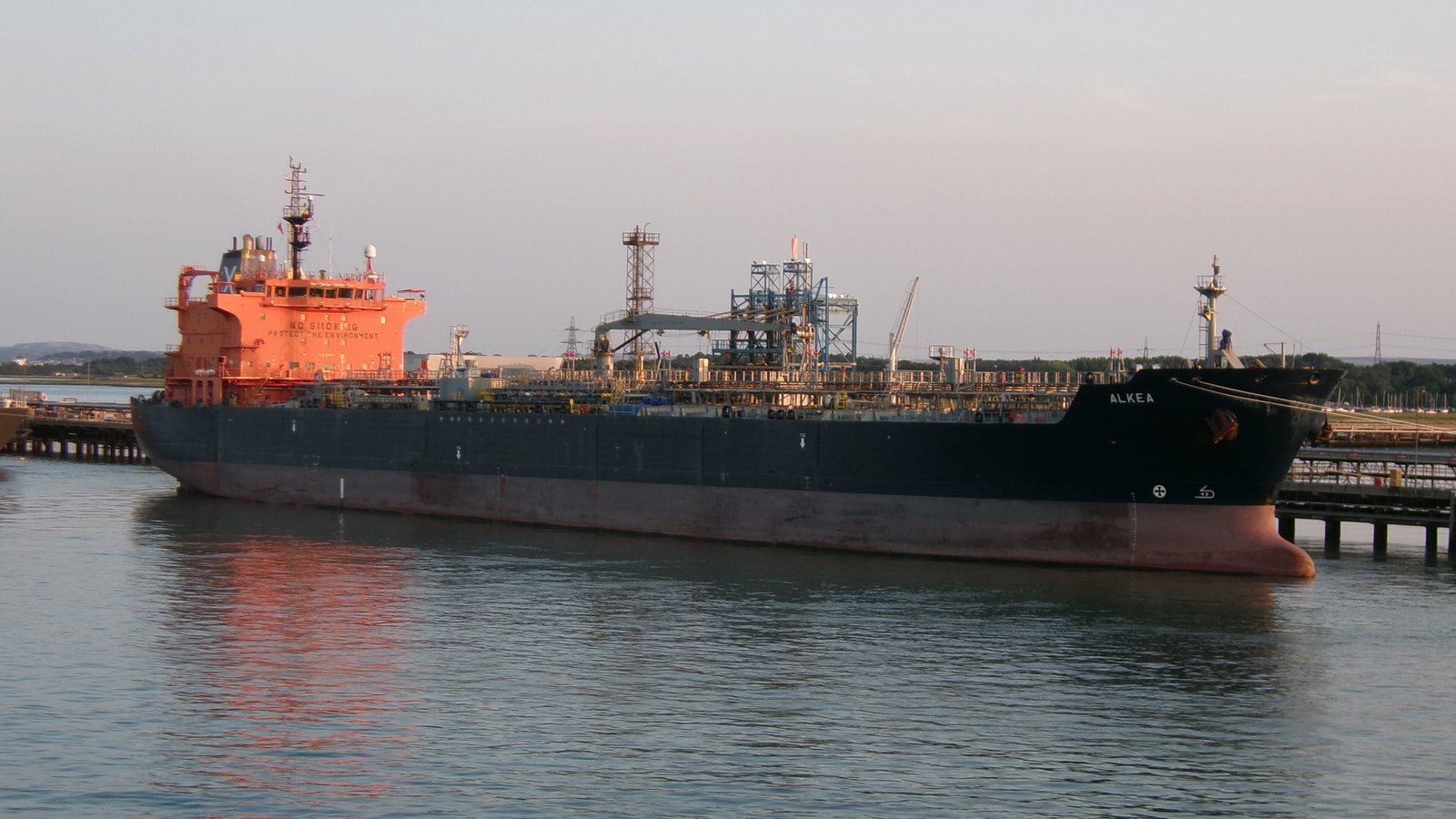 A tanker ship moored at the jetty of an oil refinery at dusk
