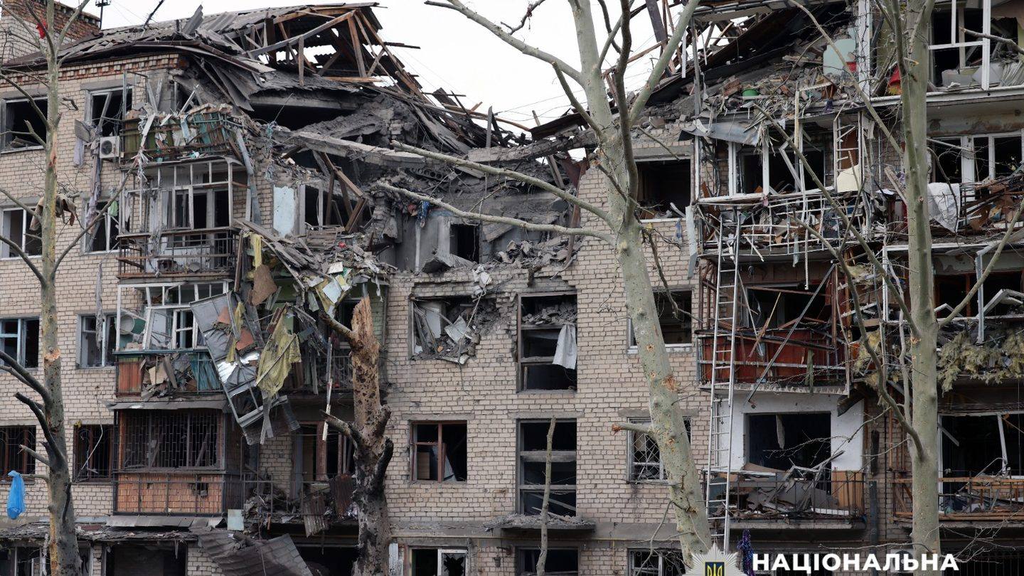 A damaged multi-storey residential building with blown-out balconies and windows in Kherson, Ukraine, behind bare trees