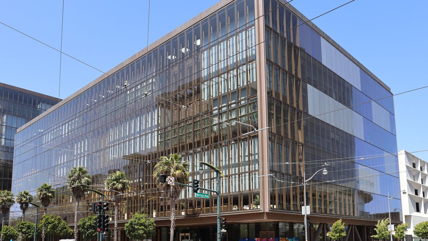 A glass-fronted office building with copper-coloured vertical fins on a corner in San Francisco's Mission Bay, under a clear blue sky