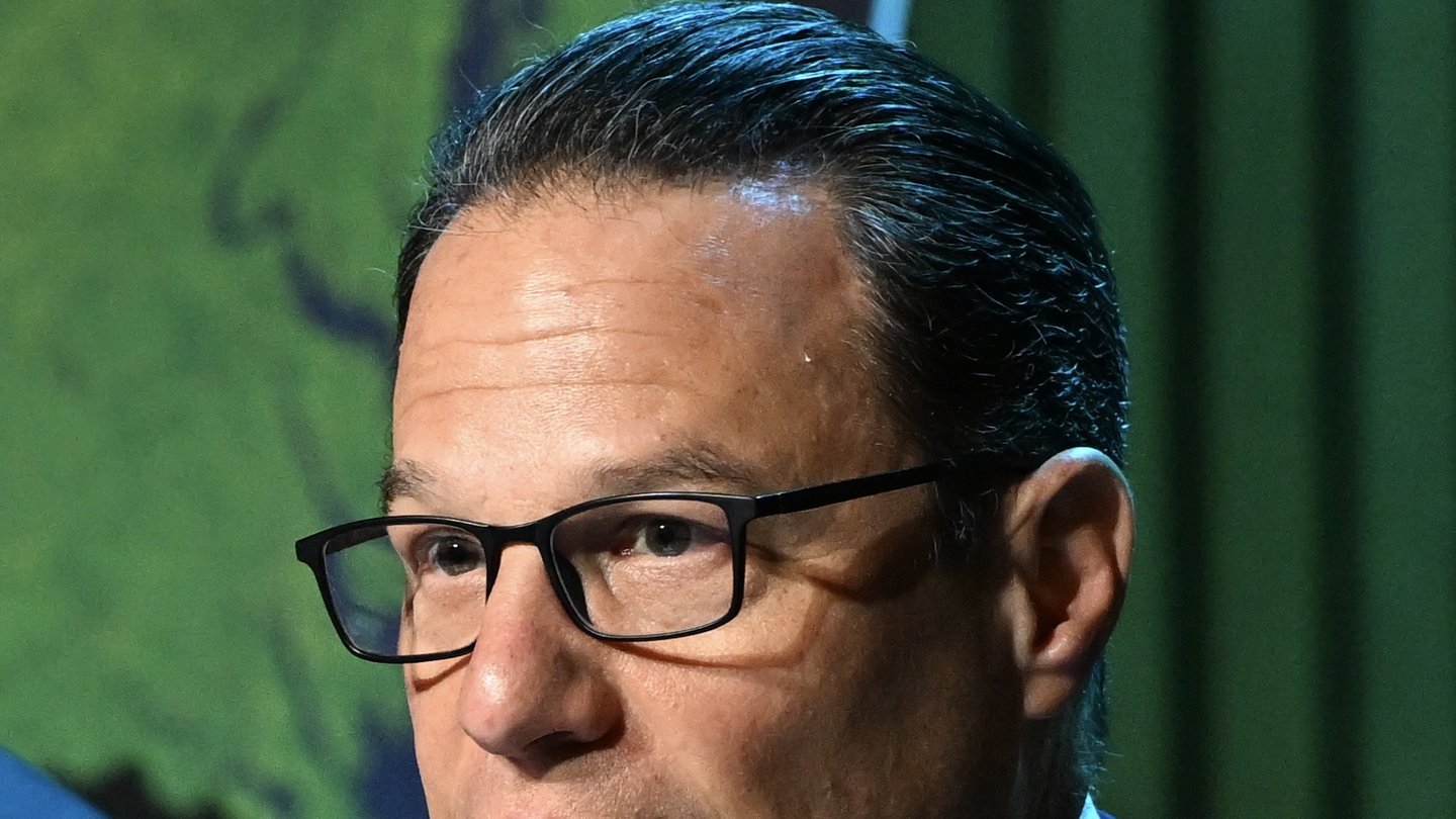 Pennsylvania Governor Josh Shapiro, wearing dark-rimmed glasses, speaking in front of a green backdrop