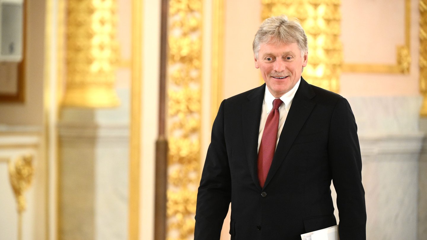 Kremlin spokesman Dmitry Peskov, in a dark suit and red tie, walks through a gilded hall in the Kremlin
