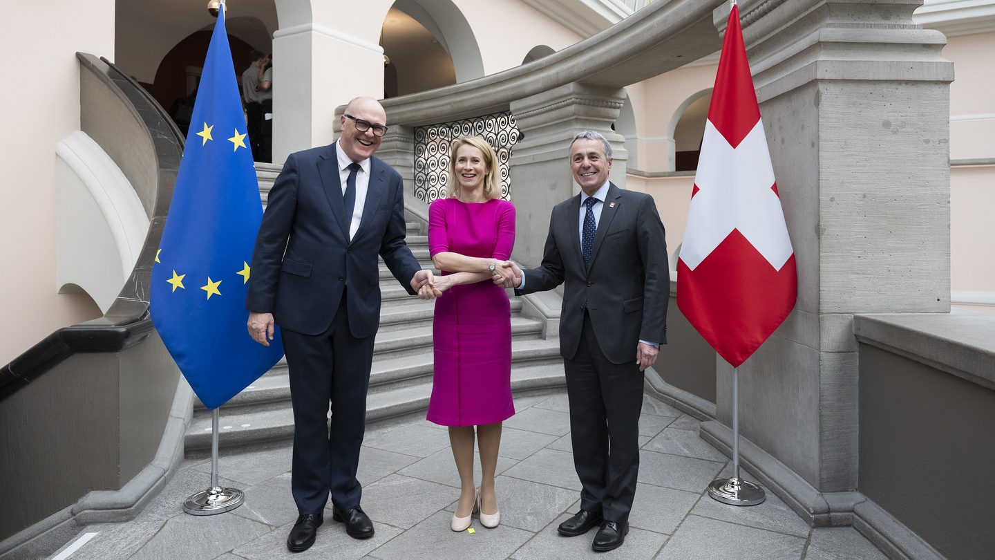 EU foreign policy chief Kaja Kallas, in a magenta dress, joins hands with two Swiss officials between an EU flag and a Swiss flag in Zurich