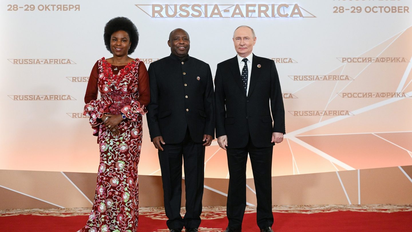 Vladimir Putin stands with Burundi's President Evariste Ndayishimiye and his wife in front of a Russia-Africa summit backdrop