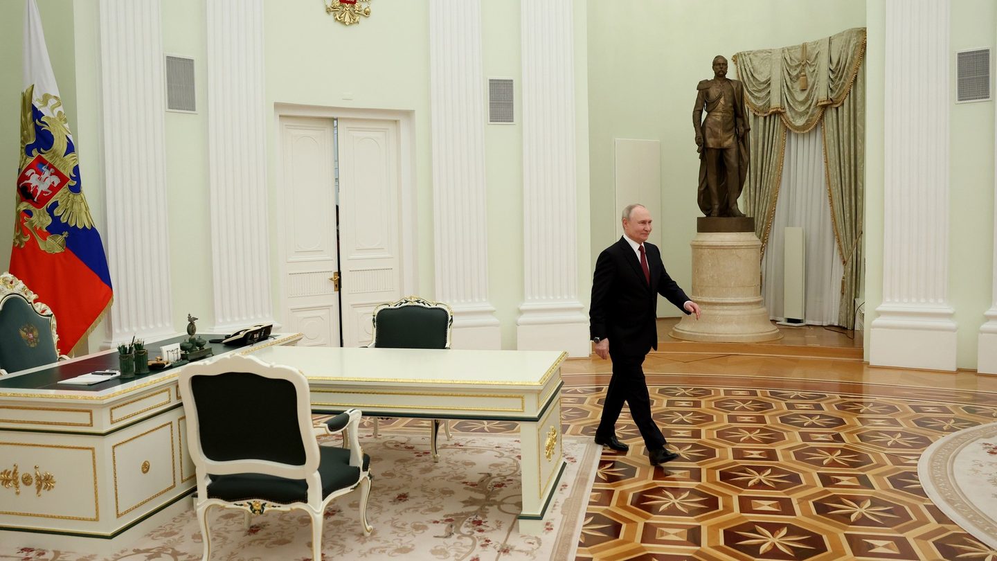 Russian President Vladimir Putin walks across a large parquet-floored hall in the Kremlin past a desk and a Russian presidential flag
