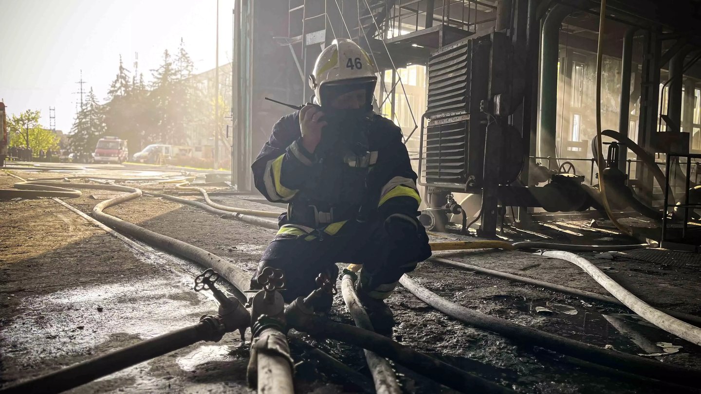 A Ukrainian firefighter in a helmet kneels among hoses inside a damaged power plant