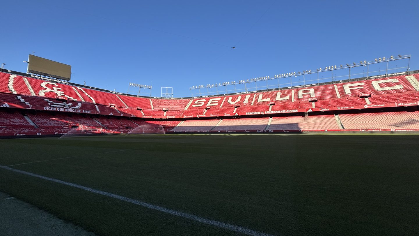 The empty red stands of Sevilla's Ramón Sánchez-Pizjuán stadium with large white letters spelling SEVILLA FC, seen from the pitch