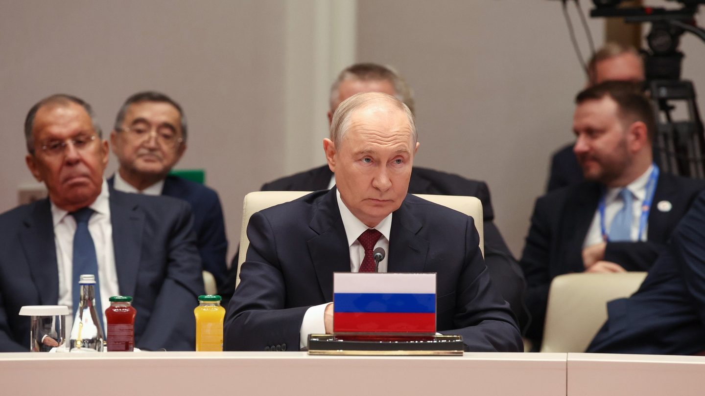 Russian President Vladimir Putin seated at a conference table behind a small Russian flag, with Foreign Minister Sergei Lavrov to his right