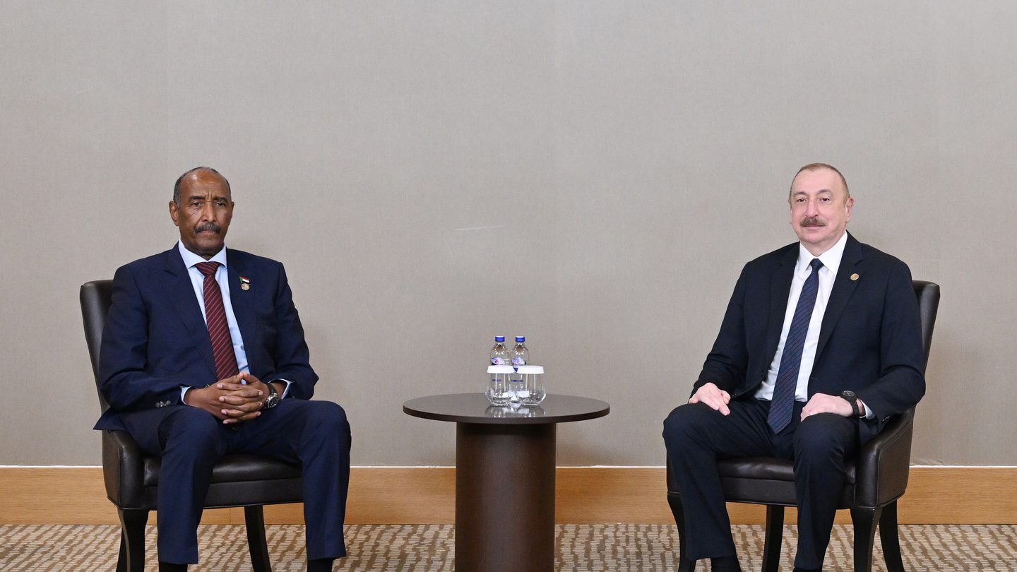 Abdel Fattah al-Burhan, in a dark suit and red tie, sits opposite Azerbaijan's President Ilham Aliyev at a small round table