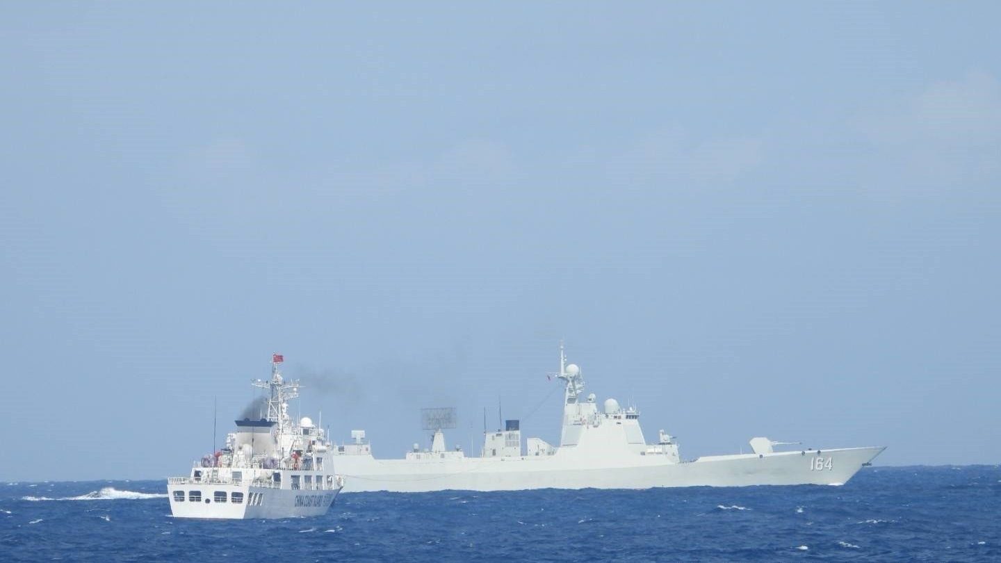 A white China Coast Guard ship sails near a grey Chinese navy destroyer with hull number 164 on open sea