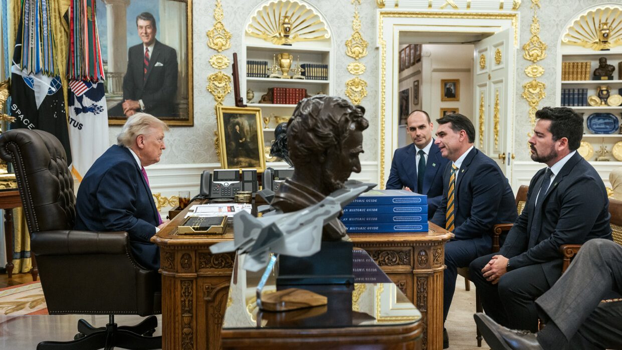 President Donald Trump sits at the Resolute Desk in the Oval Office facing Brazilian Senator Flávio Bolsonaro, his brother Eduardo Bolsonaro and Paulo Figueiredo