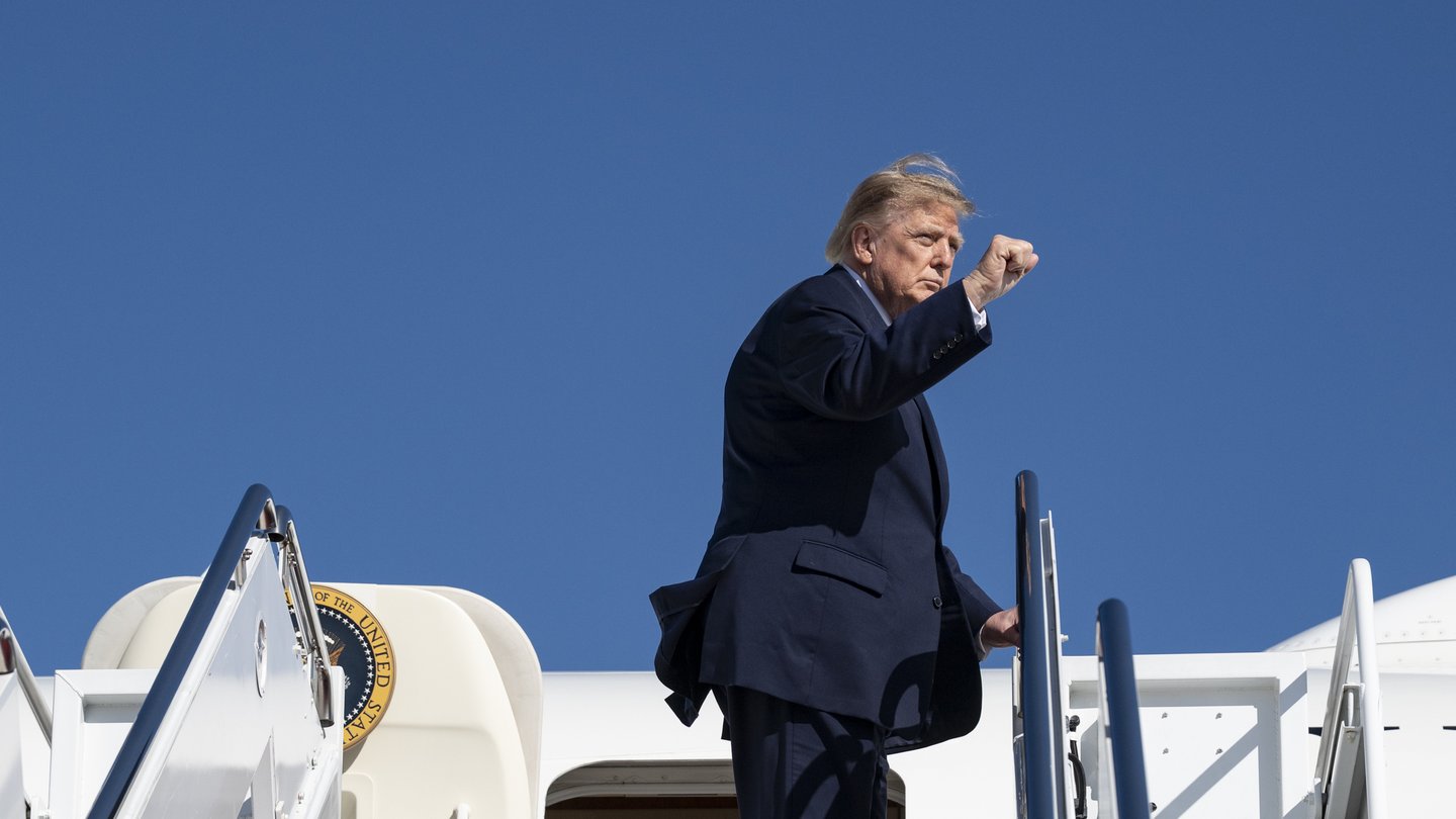 President Donald Trump raises his fist at the top of the stairs of Air Force One under a blue sky