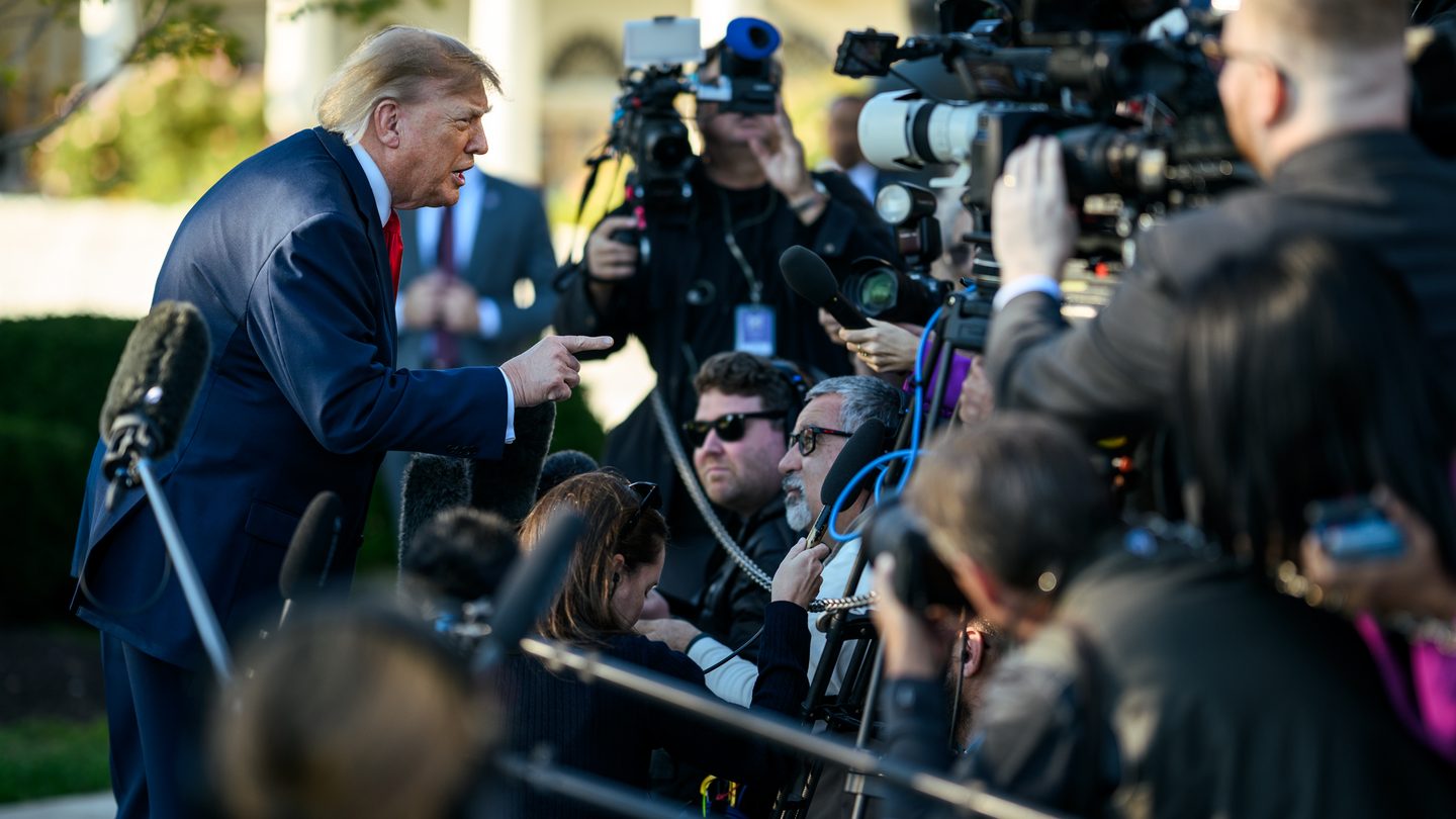 President Donald Trump in a dark suit and red tie speaks to reporters and camera crews on the South Lawn of the White House