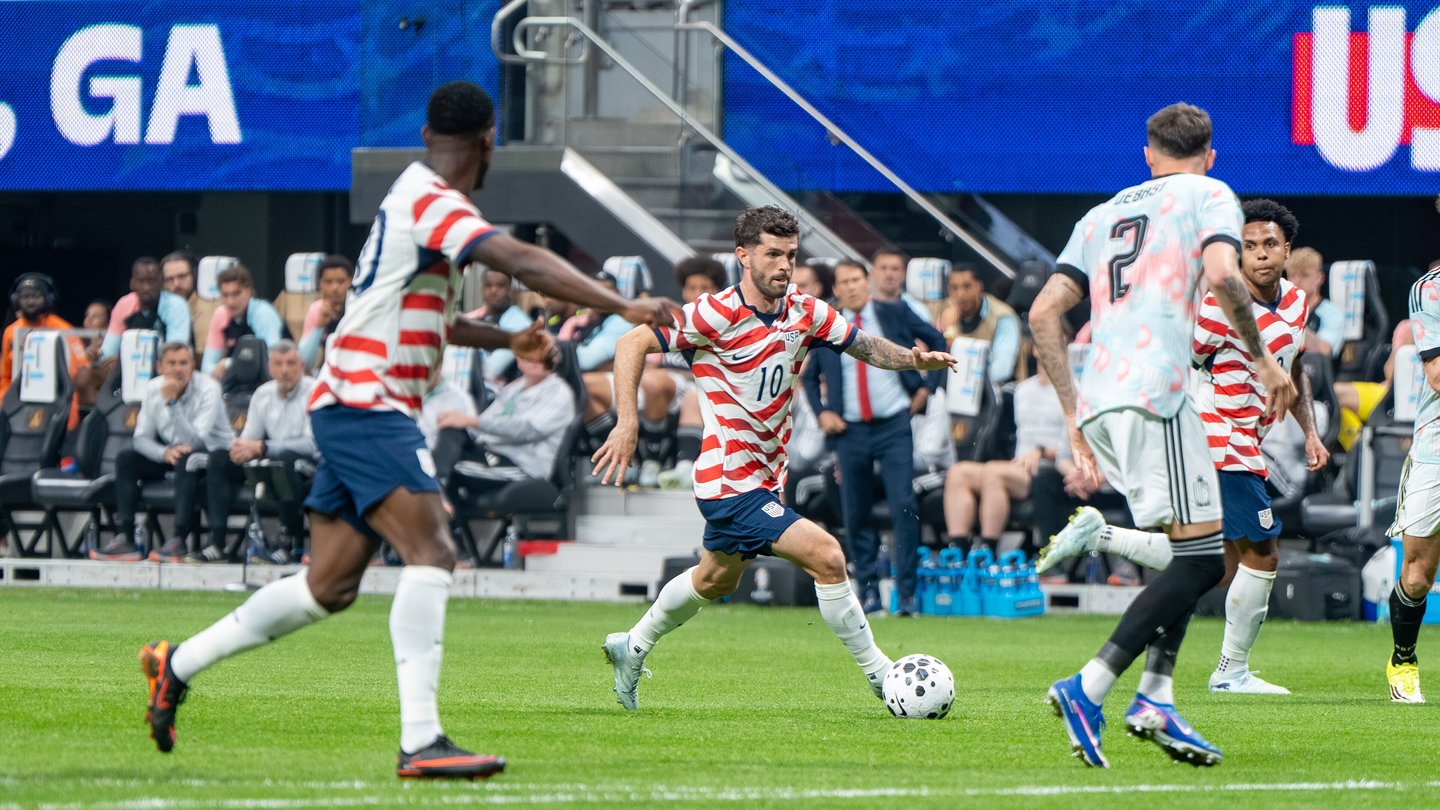 Christian Pulisic in a white and red striped United States shirt running with the ball as Belgium players in white chase