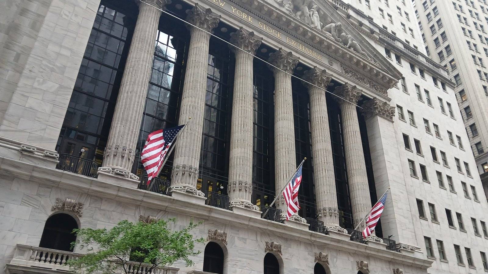 The tall columns of the New York Stock Exchange building on Broad Street with three US flags flying from the facade