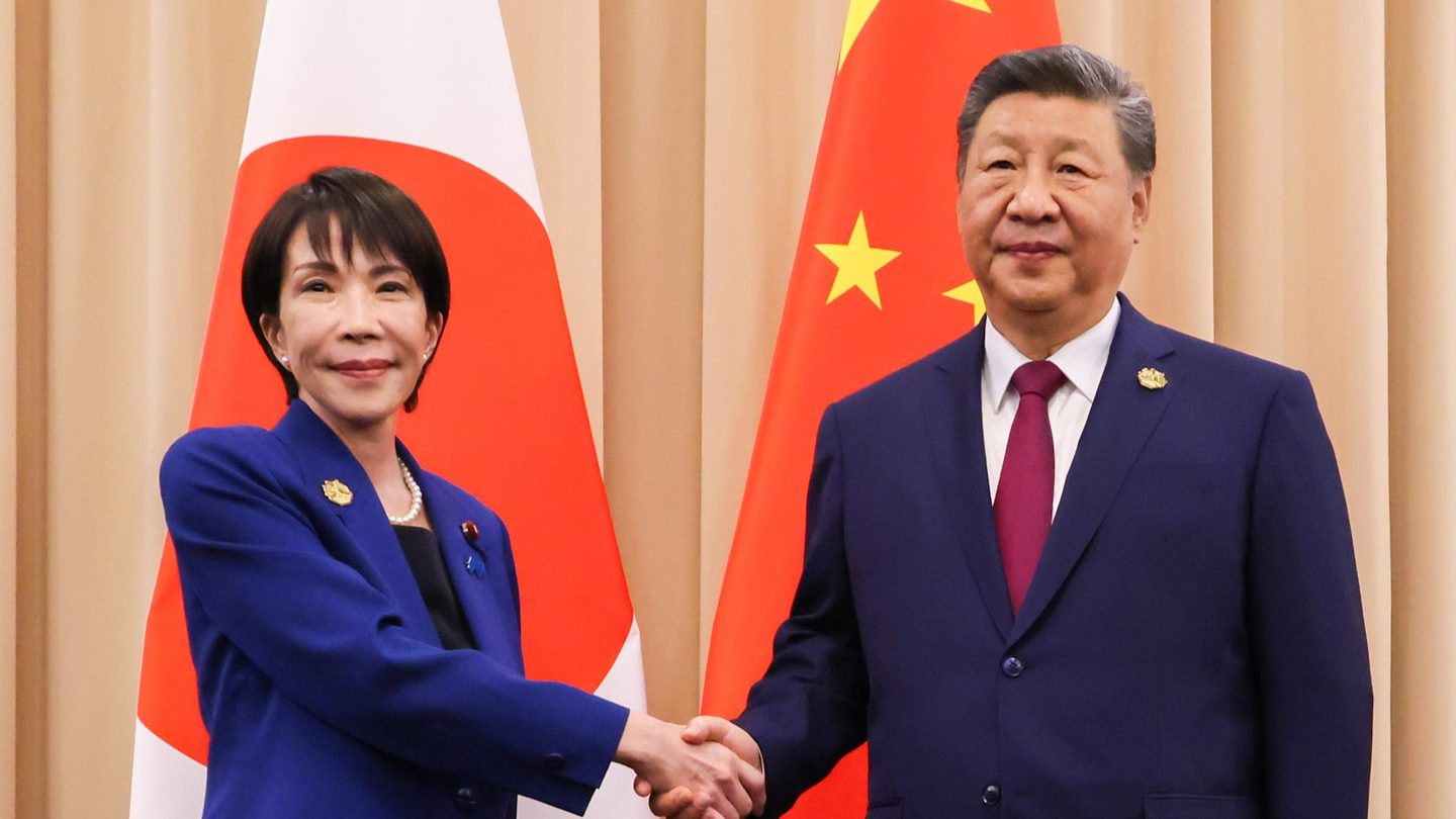 Japanese Prime Minister Sanae Takaichi shakes hands with Chinese President Xi Jinping in front of Japanese and Chinese flags