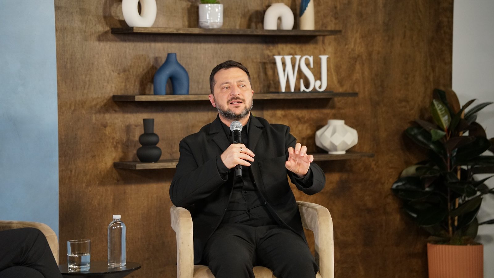 Ukrainian President Volodymyr Zelensky speaks into a microphone while seated on stage during an interview