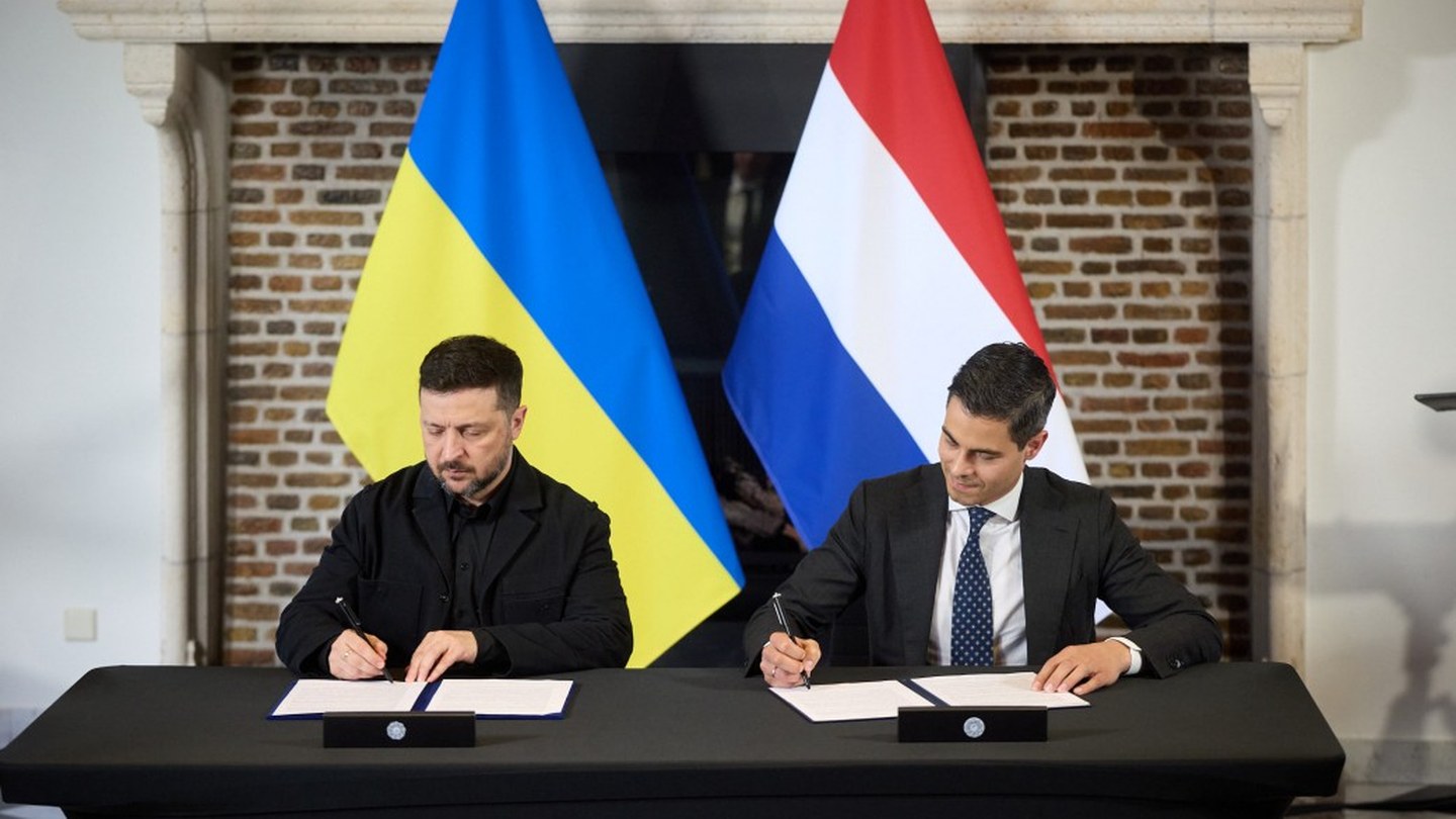 Ukrainian President Volodymyr Zelensky and Dutch Prime Minister Rob Jetten sign documents at a table in front of Ukrainian and Dutch flags